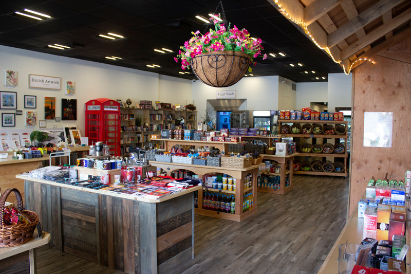 Interior view of The Hamlet British store showing shelves of British food and gifts, and a decorative hanging planter with flowers.